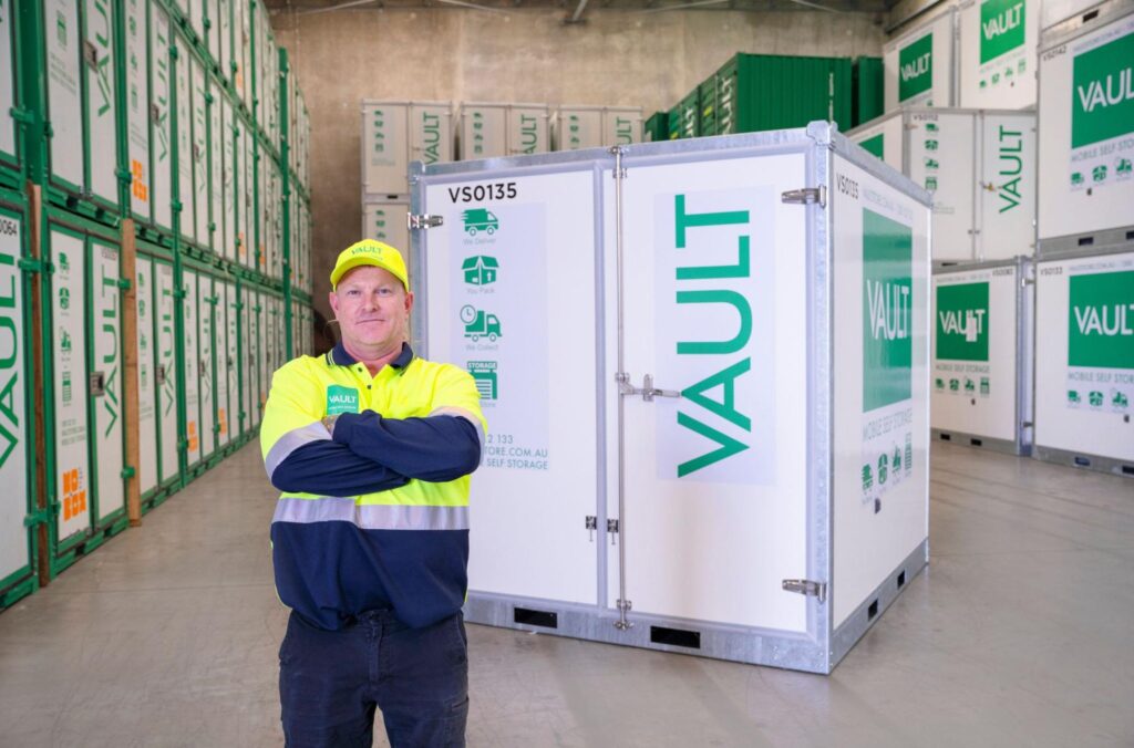A man stands confidently in front of a large storage container, showcasing its size and industrial setting.