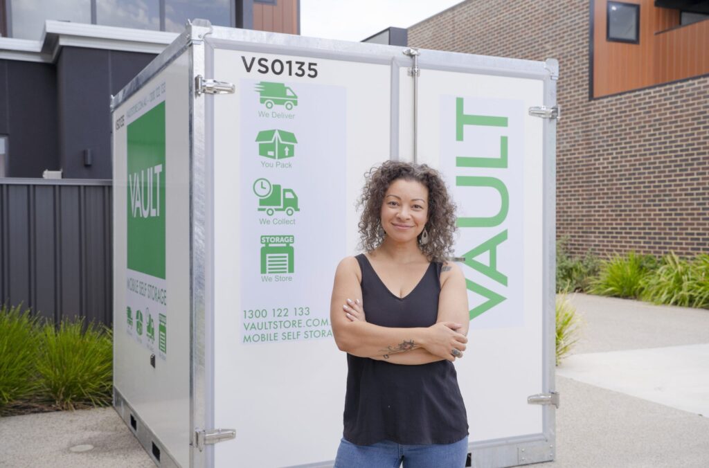 A woman stands confidently in front of a white storage container, highlighting Vault Mobile Storage's efficiency for production.