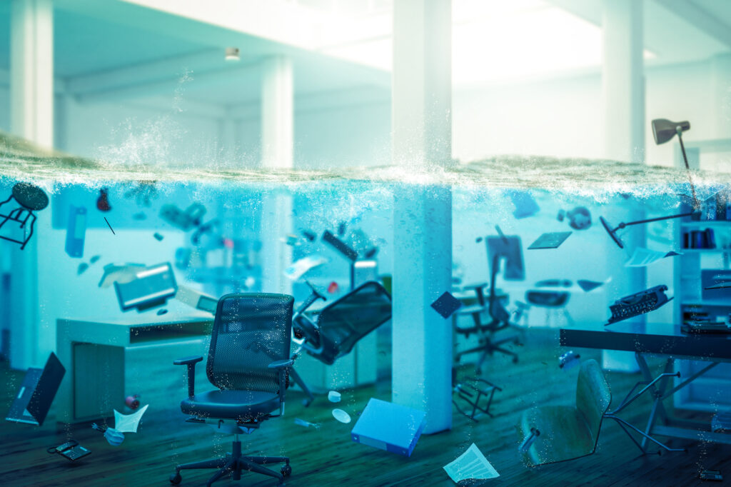 Disaster Recovery Storage illustrating a flooded office with submerged workstations and scattered equipment, highlighting business data protection.
